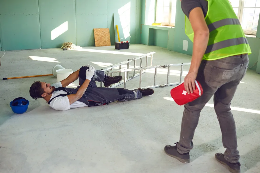 Painter lying on the ground in pain holding his knee next to a tipped-over ladder needing to call a Houston work injury lawyer.