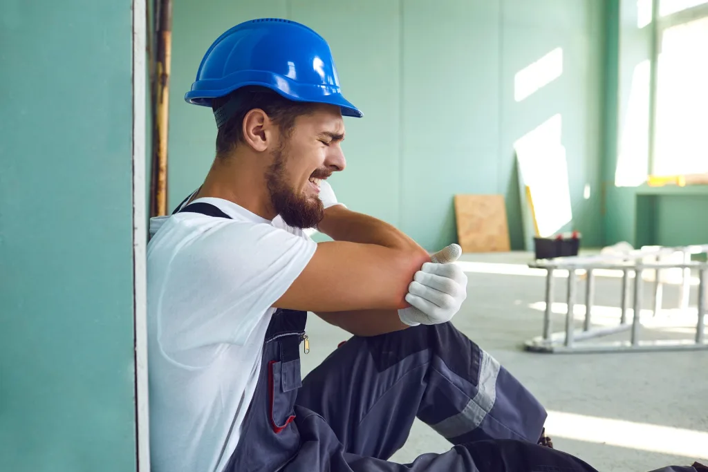 Male painter sitting on the ground crying in pain and holding his elbow. If you’ve been injured on the job, our team of job injury lawyers is ready to fight for you.