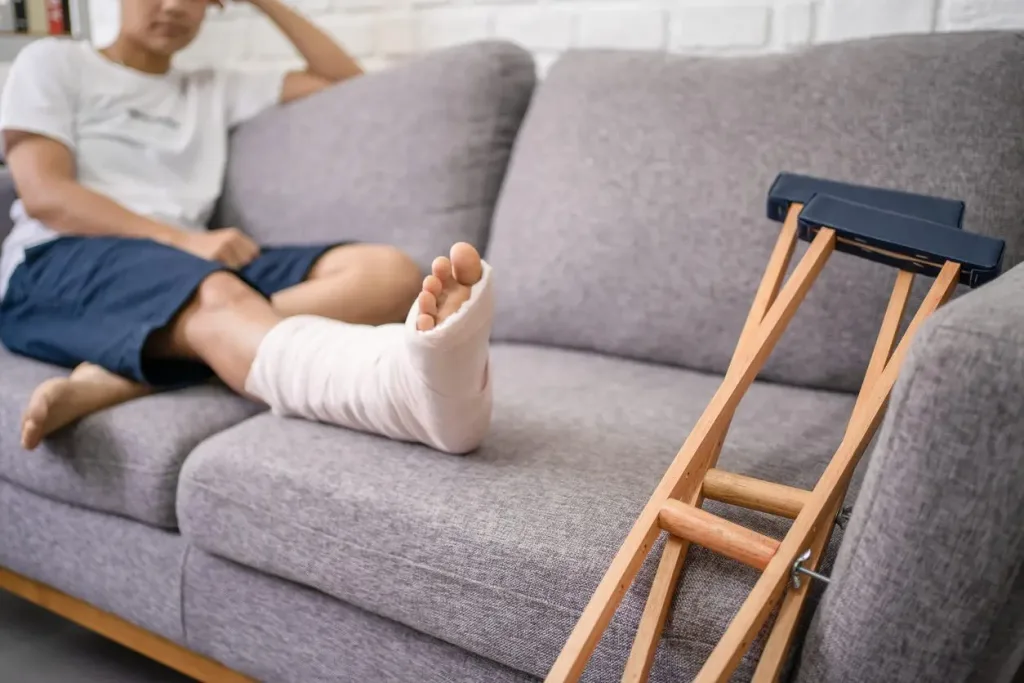 Person resting broken foot on couch next to crutches. Our personal injury lawyers know how to fight for those injured by negligence.  