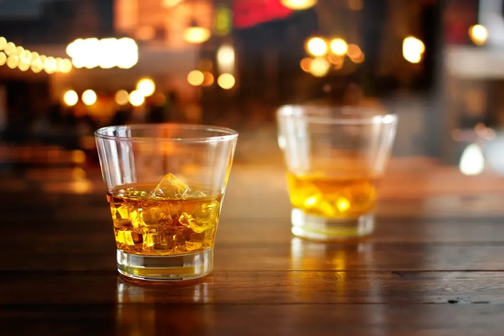 Two glasses of whiskey on a wood table. Our Houston personal injury lawyers hold dram shops accountable for acts of negligence. 