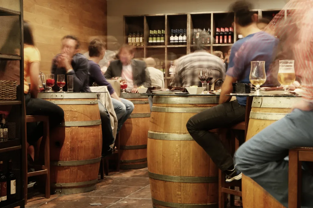 Dram whop with people who are blurry, drinking alcohol on barrels as tables.