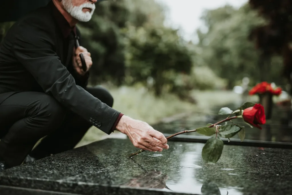 A man putting a rose on a casket.